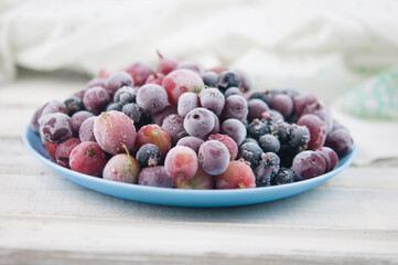 Frozen berries fruits background in ceramic plate close up.Fruits with frost. on vintage white wooden planks, blank space for text, copy space