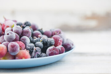 Frozen berries fruits background in ceramic plate close up.Fruits with frost. on vintage white wooden planks, blank space for text, copy space