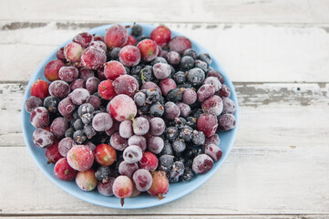 Frozen berries fruits background in ceramic plate close up.Fruits with frost. on vintage white wooden planks, blank space for text, copy space