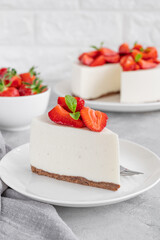 No baked cheesecake with fresh strawberries and mint on top on a white plate on a gray concrete...
