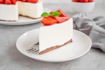 No baked cheesecake with fresh strawberries and mint on top on a white plate on a gray concrete background. Copy space.