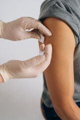 Close-up vertical shot of doctor making covid19 vaccination injection dose in shoulder. Closeup of young man getting injected with vaccine in upper arm. Closeup hands of nurse vaccinating male.