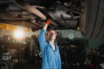 portrait of a professional female auto mechanic working under a vehicle on a lift in service. makes...