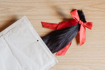 Mechón de pelo cortado anudado con un lazo de raso rojo metido en un sobre de color marrón....