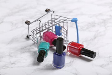 Mini shopping cart with nail polish bottles on marble backdrop