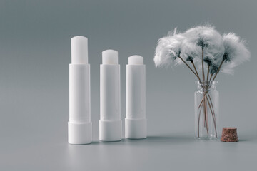 Hygienic lip balms and fluffy white flower on silver color background.