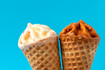 Close up of two cone ice cream with caramel and white chocolate on blue background.