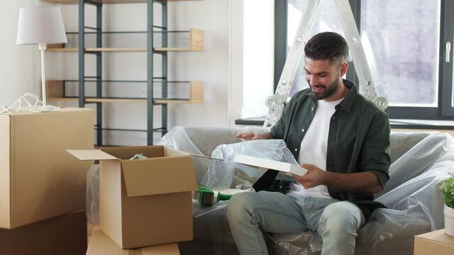 moving, people and real estate concept - happy smiling man with adhesive tape gun packing box at home