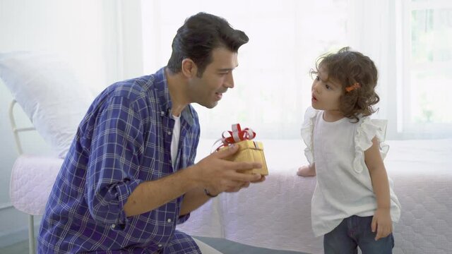 Young father sit on couch make birthday surprise to excited cute preschooler daughter, happy little girl child amazed by gift box present by dad