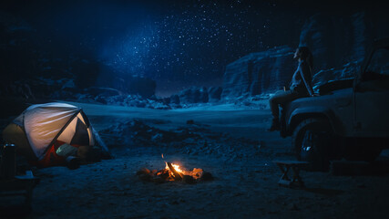 Female Traveler Sitting on Her SUV hood Watching Night Sky while Camping in the Canyon by Campfire....