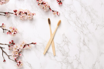 Eco bamboo toothbrushes and beautiful white flowering branches on marble background. Springtime, eco concept. Flat lay, top view.