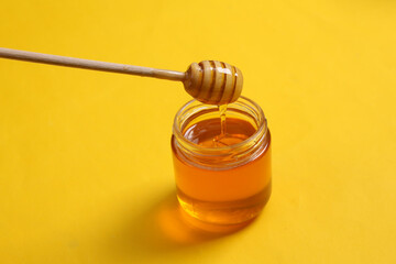 Jar of honey bee with spoon on yellow background.