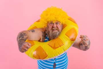 Fat angry man with wig in head is ready to swim with a donut lifesaver