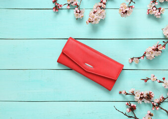 Red Purse and beautiful flowering branches on blue wooden background. Springtime, beauty concept. Flat lay, top view.