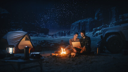 Happy Couple Nature Camping in the Canyon at Night, Use Laptop Computer, Sitting by Campfire. Two...