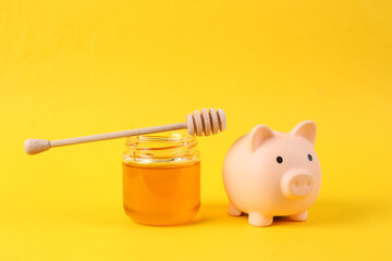 Piggy bank and Bee honey jar with honey wooden spoon on yellow background