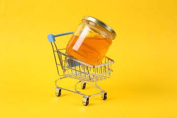 Mini shopping trolley with Bee honey jar on yellow background