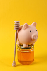Piggy bank and Bee honey jar with honey wooden spoon on yellow background