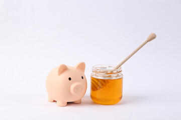 Piggy bank and Bee honey jar with honey wooden spoon on white background
