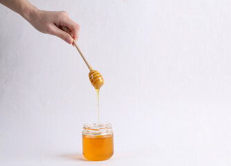 Hand holds honey spoon with jar of bee honey on white background