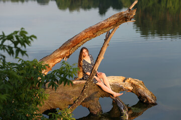 Young long haired woman sitting on a snag in the lake