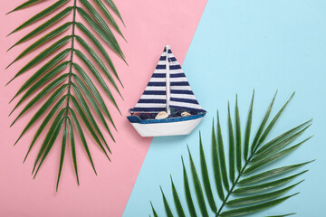 Saiboat and palm leaves on pink blue background. Tropical composition. Top view. Flat lay