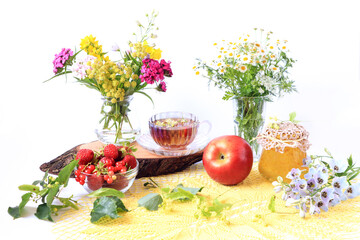 The concept of harvesting in the summer season. Ripe berries and fruits, a jar of jam, lime branches on a yellow napkin, light background, side view