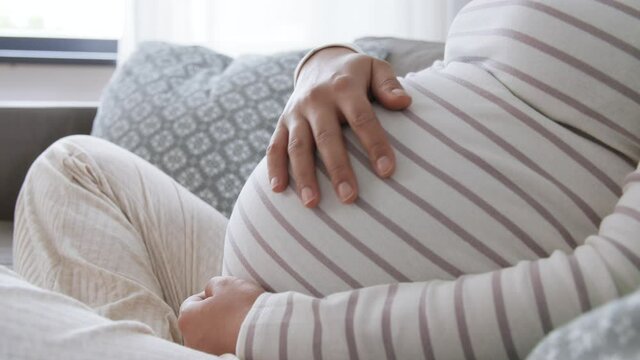 pregnancy, rest, people and expectation concept - happy smiling pregnant asian woman sitting on sofa at home