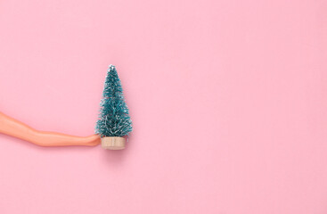 Doll hands holding Christmas tree on pink pastel background. Minmalism, concept art.