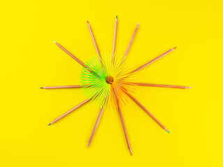 Colorful rainbow spiral toy and color school crayons on yellow background