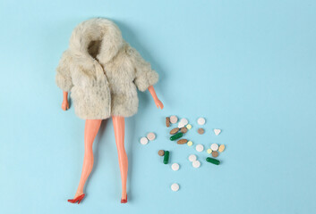 Overdose, drug addiction. Lot of pills and doll in fur coat on blue background. Minimalism
