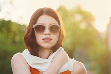 Young beautiful woman in stylish sunglasses posing and looking at camera. Pretty girl walking outdoors..