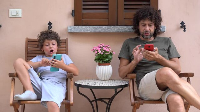 father and son spend time in front of the mobile phone online on the internet - addiction to social networks by adults and children