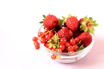 Ripe strawberries and red currants in a glass cup on a white background, side view, space for text