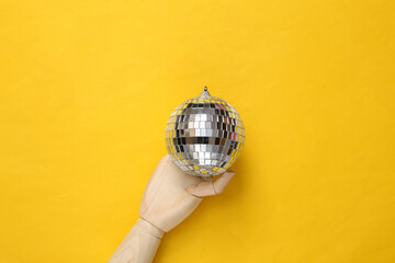 Wooden hand holding Disco ball on yellow background. Top view. Flat lay. Minimalism party concept