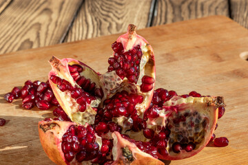 Ripe pomegranate, broken into five parts. On a wooden background.