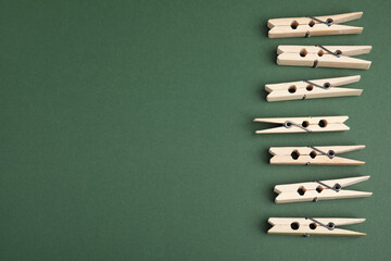 Wooden clothespins on dark green background, flat lay. Space for text