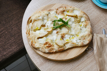 Roman round pizza five or four cheeses with baked pear on a round wooden kitchen pizza board. Delicious fresh Italian pizza on a round wooden table. Selective focus