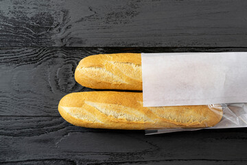 French bread mini baguette on an old black, dark wooden table in a white paper bag. Rustic...