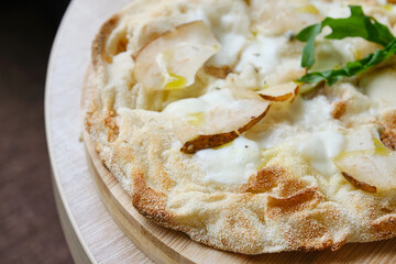 Roman round pizza five or four cheeses with baked pear on a round wooden kitchen pizza board....