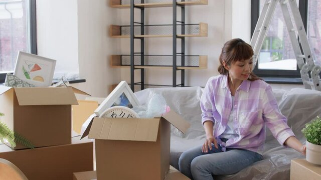 moving, people and real estate concept - happy smiling asian woman unpacking boxes at new home