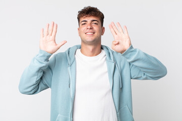 young handsome man smiling and looking friendly, showing number nine or ninth with hand forward,...