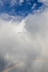Fototapeta na wymiar Rainbow and rainy gray white blue sky with fluffy clouds