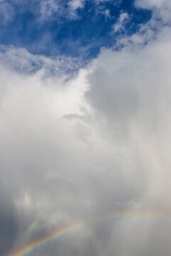 Rainbow and rainy gray white blue sky with fluffy clouds © kvitkanastroyu