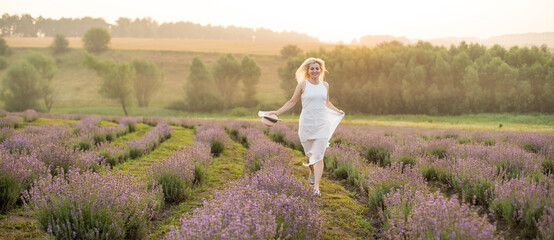 Beautiful young woman wearing a white dress walking in the middle of a lavender field in bloom