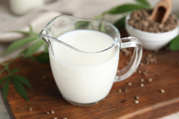 Glass jug with fresh hemp milk on wooden board, closeup