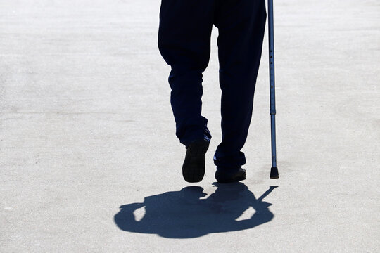 Silhouette of man walking with a cane down the street, shadow on asphalt. Concept of old age, diseases of the spine or joint disease, elderly people