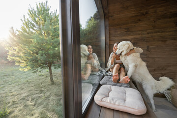 Young woman resting at beautiful country house or hotel, sitting on the window sill with pine...