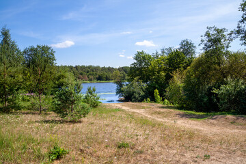 A sandy road among grass and green trees to the Narva River in Estonia on a sunny day under the blue sea.
