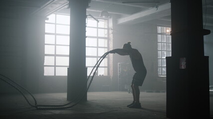 Fototapeta na wymiar Guy battling ropes during training session. Sportsman performing intense workout